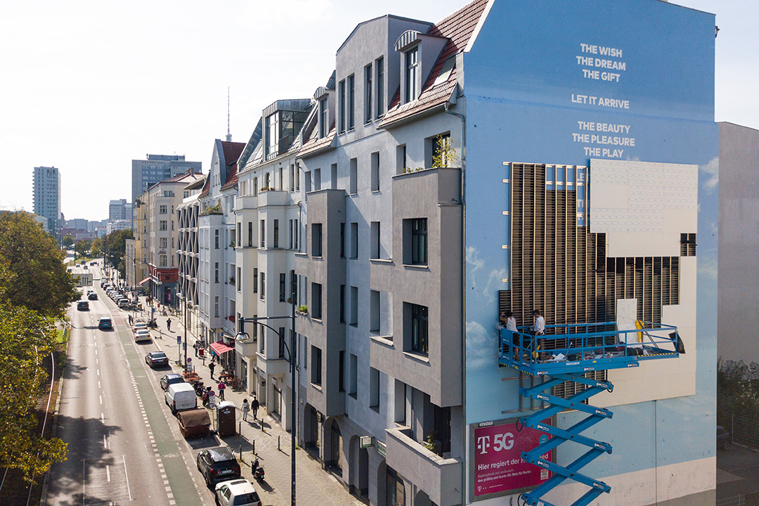 An aerial view of the street with the mural wall partly complete and a scissor lift beside it